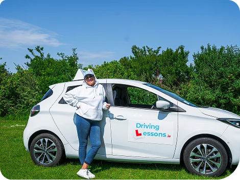 Woman_wearing_a_white_hoodie_stands_next_to_a_car_ISM_Driving_lessons