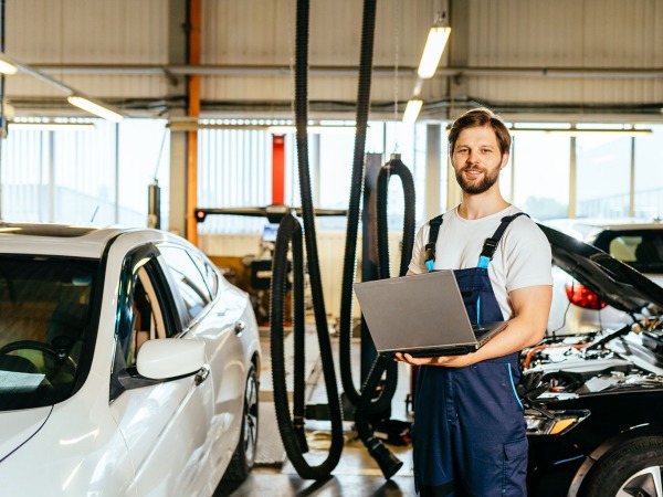 A_man_stands_holding_a_laptop_in_front_of_a_parked_car _ISM_Training_and_Recruitment